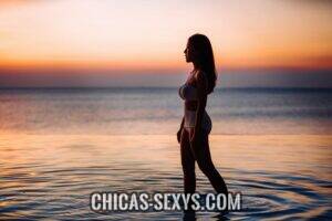 Aplicaciones de citas: Chica hermosa caminando en bikini con los pies en el agua. Ella esta esperando encontrar una pareja en línea para poder disfrutar de ese momento.